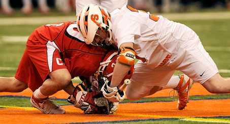 2 players facing off one in a red uniform the other in a white uniform standard equipment is regulated lacrosse ball lacrosse stick and regulated protective gear