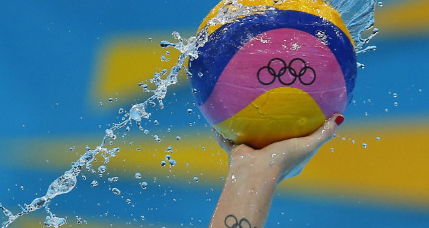 olympic water polo ball in the air with water flung around it polo player with olympic tattoo on wrist official olympic water polo ball