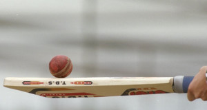 A cricket ball is resting on top of a cricket bat these are the regulated cricket ball and bat