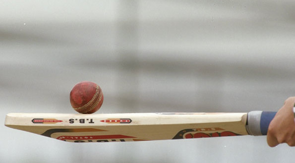 A cricket ball is resting on top of a cricket bat these are the regulated cricket ball and bat