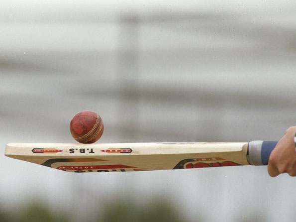 A cricket ball is resting on top of a cricket bat these are the regulated cricket ball and bat