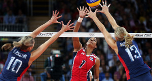woman in red spiking the ball while 2 women in blue try to block the ball basic equipment for volleyball ball is a regulated ball