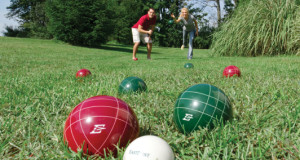 2 people playing bocce ball in a grassed area 2 green balls 3 red balls one white ball basic equipment bocce ball bocce ball set with different colored balls