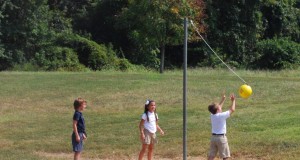 school kids playing tetherball yellow ball equipment on string on a pole with 2 kids playing and one kid watching