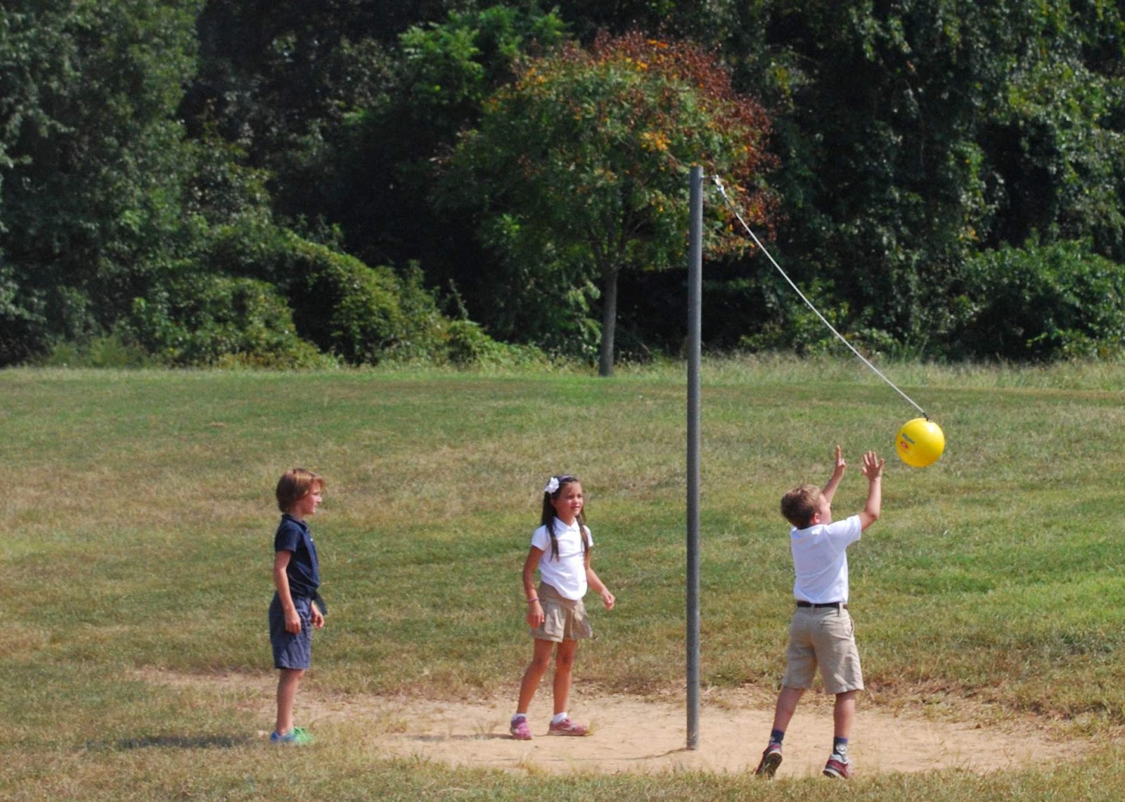school kids playing tetherball yellow ball equipment on string on a pole with 2 kids playing and one kid watching