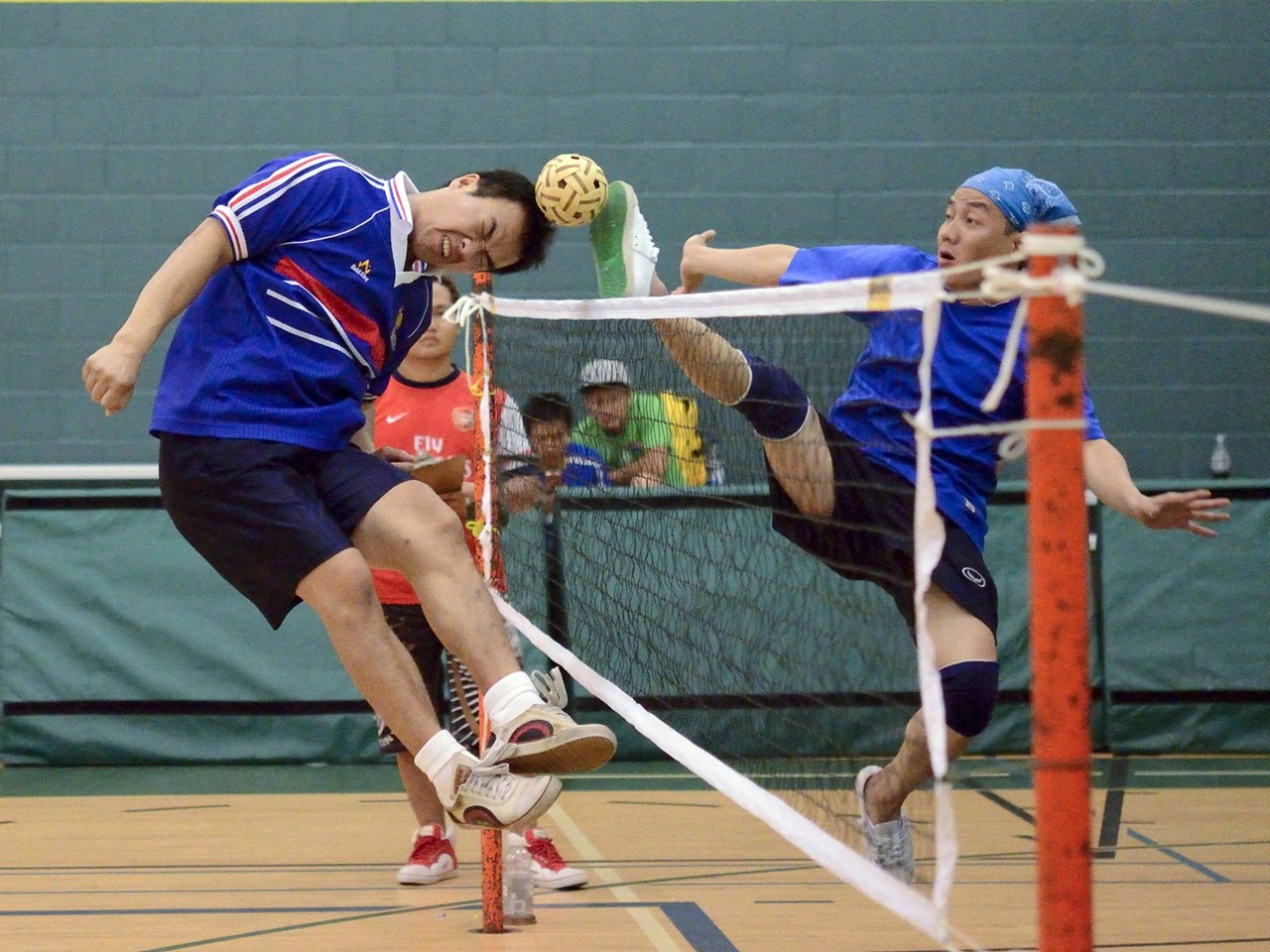 sepak takraw game one opponent is head budding the ball while the other is kicking the ball over a net that is similar to a volleyball net standard equipment for sepak takraw