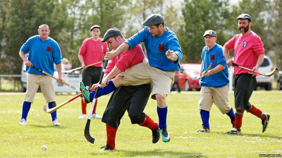 Shinty game with 3 men on blue team and 3 men on red team regulated equipment for shinty