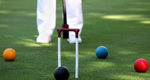person in white pants standing behind a croquet game with orange/yellow ball black ball blue ball and red ball standard equipment for croquet