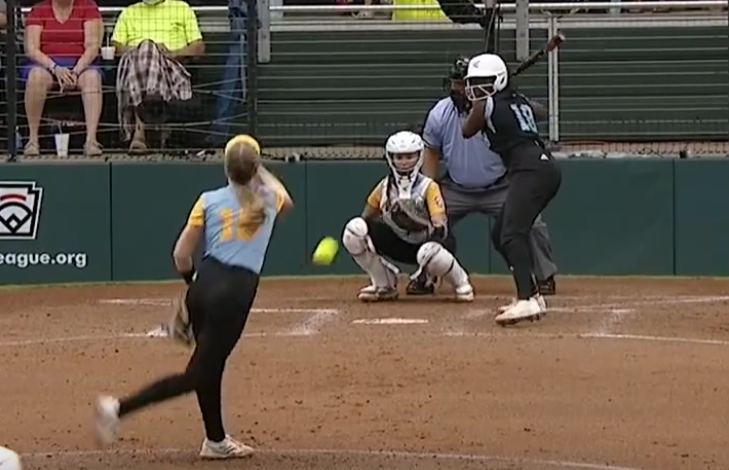 Little League Softball ball in flight from pitcher to batter, with catcher poised to stop the ball.